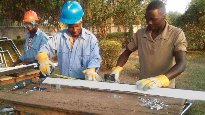 3 men wearing TAG Fabrications overalls, scaling steel and aluminium materials in Uganda